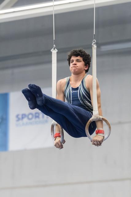 Young gymnast performing L-sit position on still rings, displaying focus and control during training