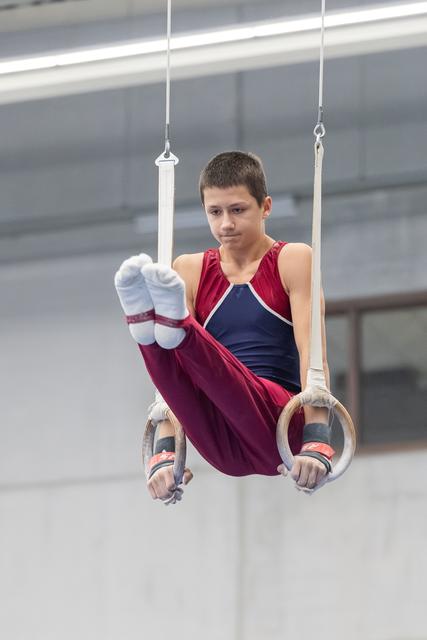 Young gymnast performing an L-sit position on rings, demonstrating focused concentration and core strength in training facility