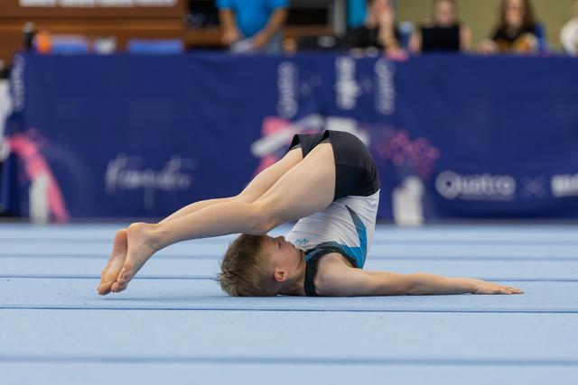 Young male gymnast performs an extreme pike backbend on the floor exercise mat during a gymnastics competition.
