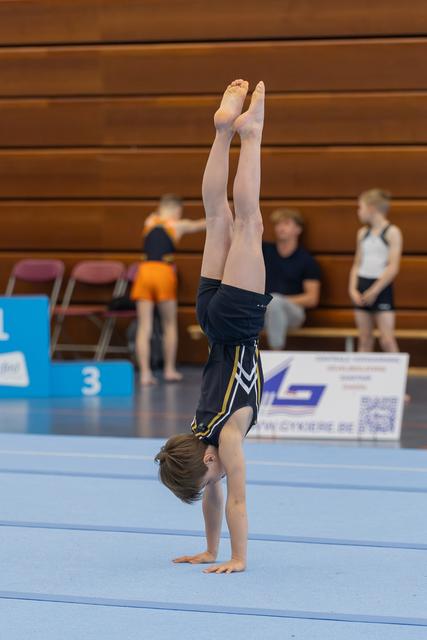 Young boy performs a perfect handstand on the floor exercise mat during an indoor gymnastics competition.