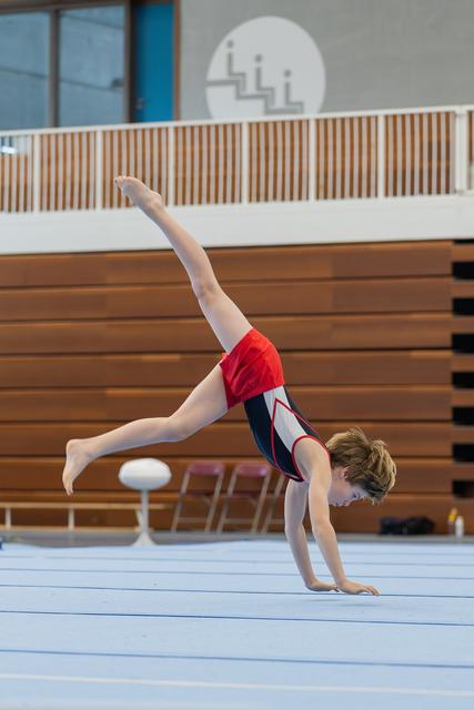 Young male gymnast performs an arabesque on the floor exercise mat, arms low, one leg raised high, intense focus.