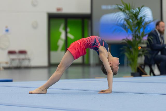 Young gymnast performs a precise bridge pose on the blue floor mat, showcasing flexibility and focus during a gymnastics event.