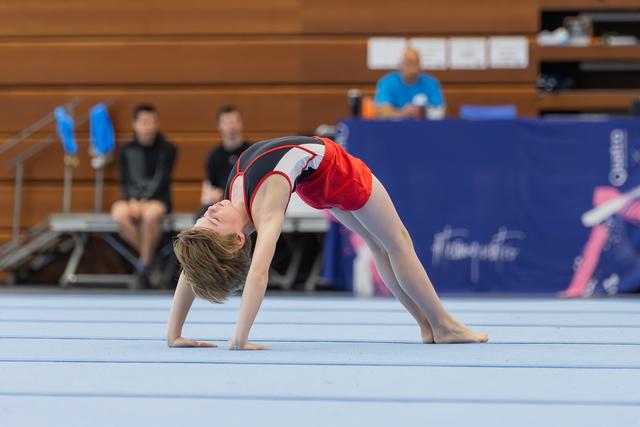 Young gymnast performs a back bridge on the floor, head tilted back, focused during a gymnastics meet.