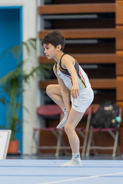 Young male gymnast crouches in concentration on the floor exercise mat, poised and focused before a routine.