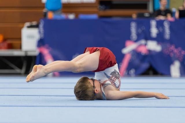 Young male gymnast performs an impressive backbend on the blue floor mat during a gymnastics meet.