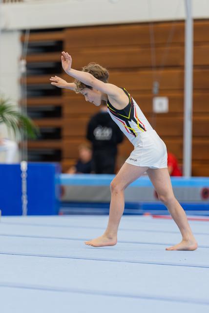 Young gymnast strikes a focused pose on the floor exercise mat, arms raised mid-routine in a gymnastics hall.