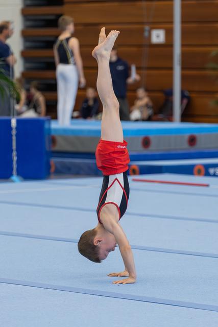 Young boy holds a perfect handstand on the floor mat, focused and controlled, during a gymnastics competition.