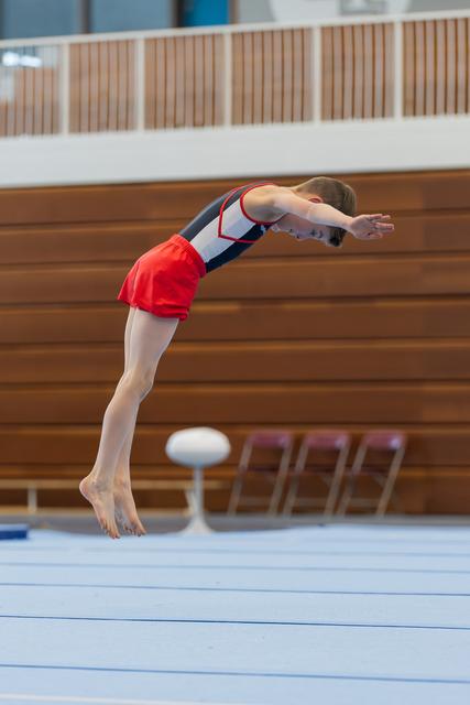 Young gymnast executes a powerful dive roll, body arched and arms extended, mid-air above the floor exercise mat.