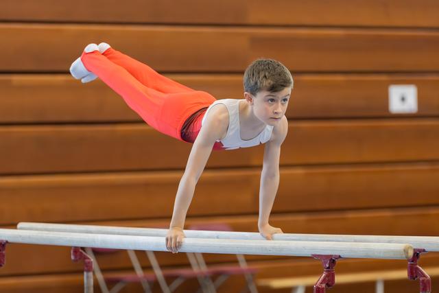 Young male gymnast holds a planche on parallel bars, body horizontal, expression intense and concentrated in a gymnasium.