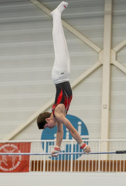 Young male gymnast performs a perfect handstand on the high bar, body fully extended, in an indoor gymnastics hall.