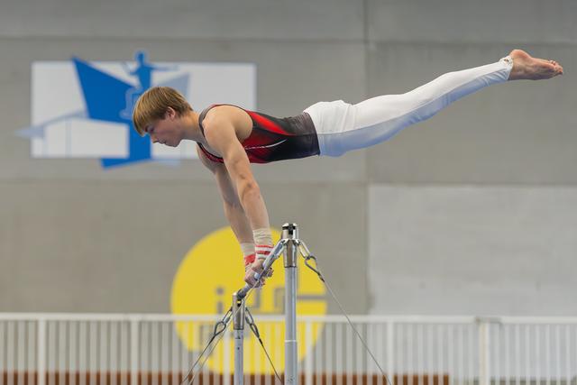 Young male gymnast holds a perfect horizontal iron cross position on the high bar, body fully extended, focused expression.