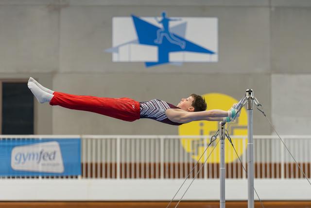 Young male gymnast performs a perfect horizontal iron cross hold on the high bar, body rigid with focused intensity.