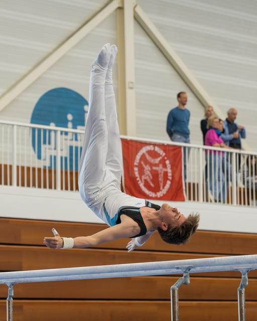 Male gymnast performs a dramatic horizontal hold on parallel bars, body fully extended, intense focus during competition.