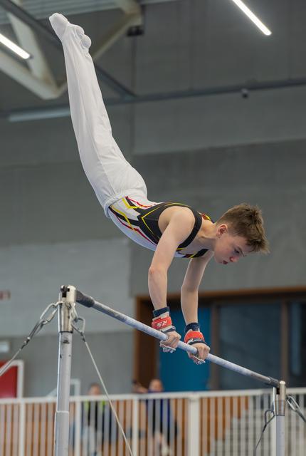 Young male gymnast performs a stunning inverted pike hold on the high bar, showing intense focus and strength indoors.