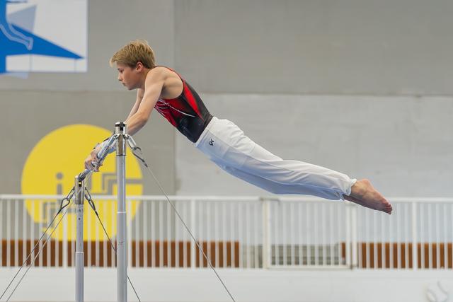 Young male gymnast holds a perfect horizontal lever on parallel bars, body fully extended with focused determination.