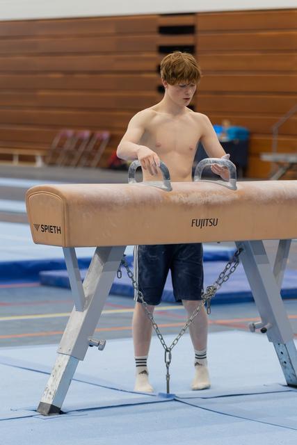 Red-haired teen gymnast focuses intently while gripping the pommel horse handles, dusting chalk in a gymnasium.