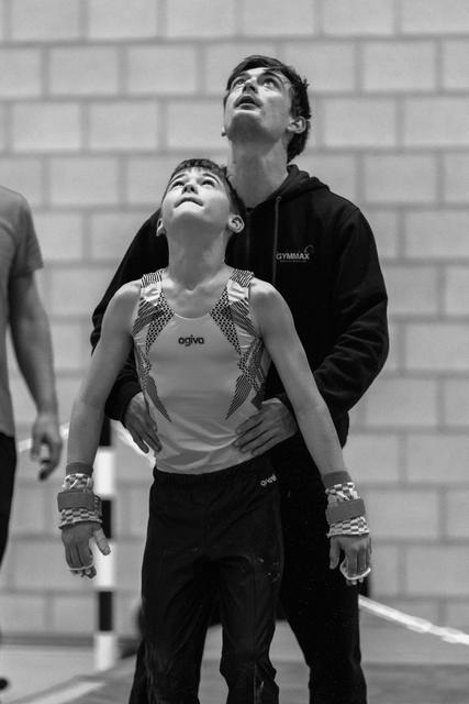 Female gymnast in decorated leotard and male coach both gazing upward intently in gymnasium, anticipating results