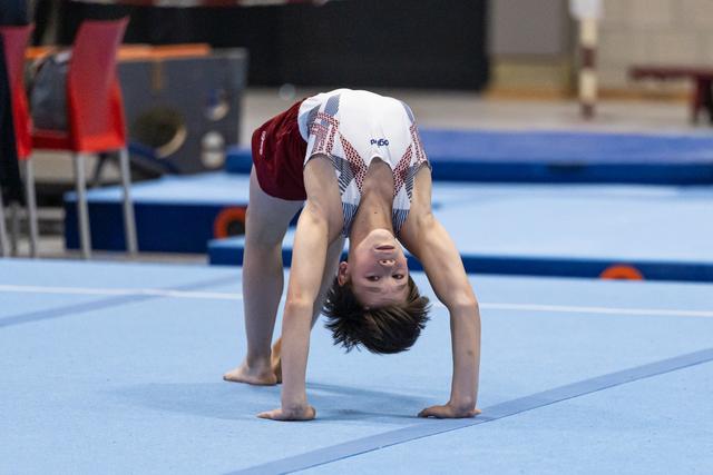 Young gymnast performs a backbend on floor mat during practice, demonstrating flexibility and control in training facility