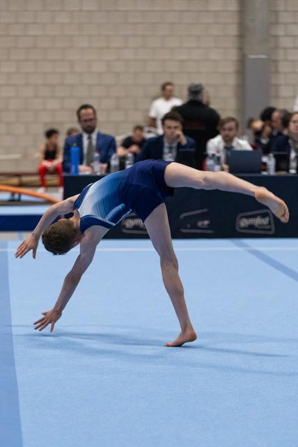 Gymnast performs graceful backbend during floor exercise, arching backwards with hands reaching toward mat