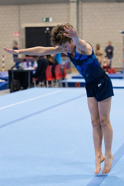 Young gymnast performs an artistic pose during floor routine, arms extended and head tilted, demonstrating grace and control