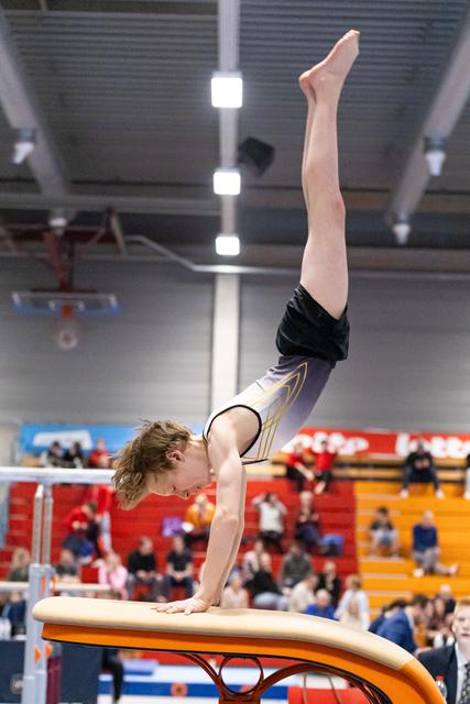 Gymnast performing perfect handstand on vault table during routine, legs extended vertically in indoor arena