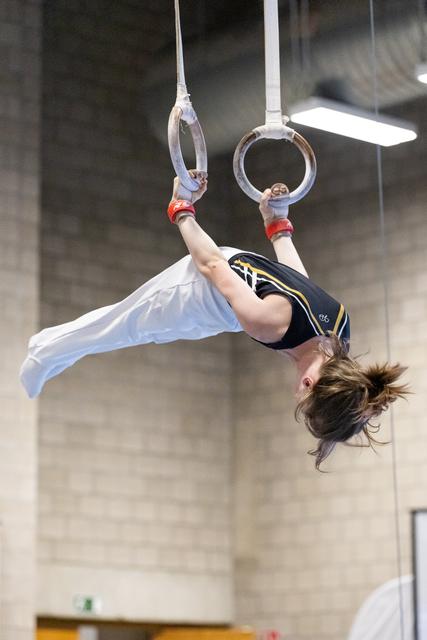 Young gymnast performs an inverted pike position on rings, demonstrating strength and flexibility during training