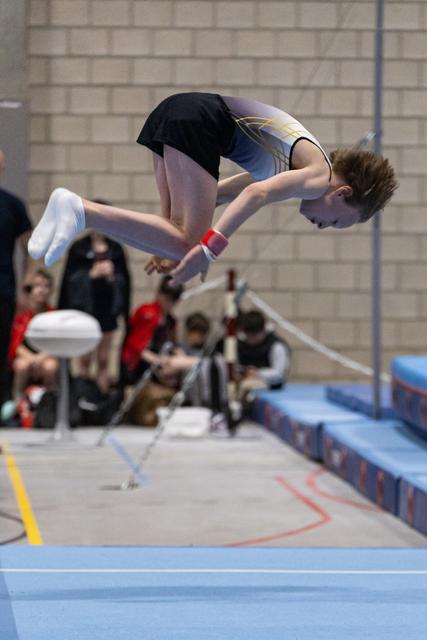 Gymnast performs inverted somersault over vault table, body tucked tightly in mid-air during indoor gymnastics event