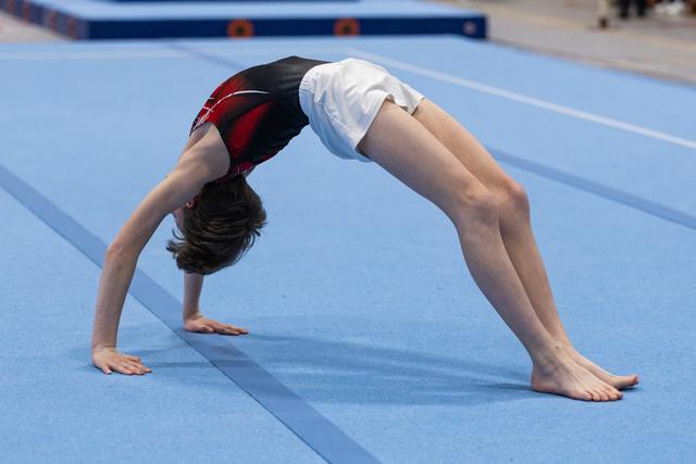 Young gymnast executing a bridge pose on blue mat, demonstrating flexibility with arched back and straight legs
