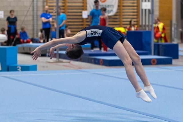 Young gymnast executing a backward aerial flip on floor exercise, displaying impressive flexibility and form during routine