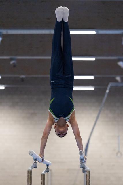 Gymnast executing a vertical handstand on parallel bars, legs straight and pointed, demonstrating balance and control