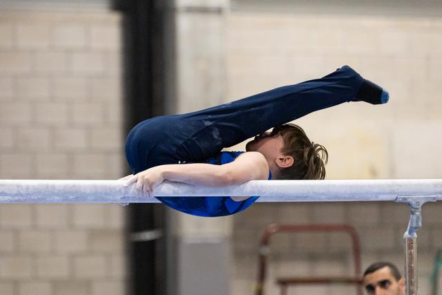 Gymnast executes a pike position on uneven bars, body folded sharply with legs extended upward during routine
