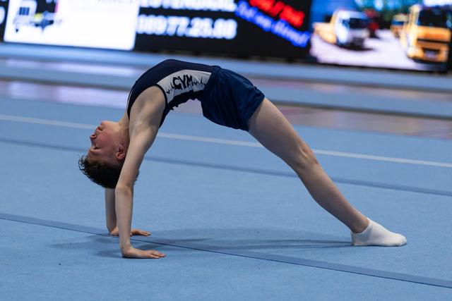 Young gymnast executes a deep backbend bridge position during floor routine, demonstrating exceptional flexibility and control