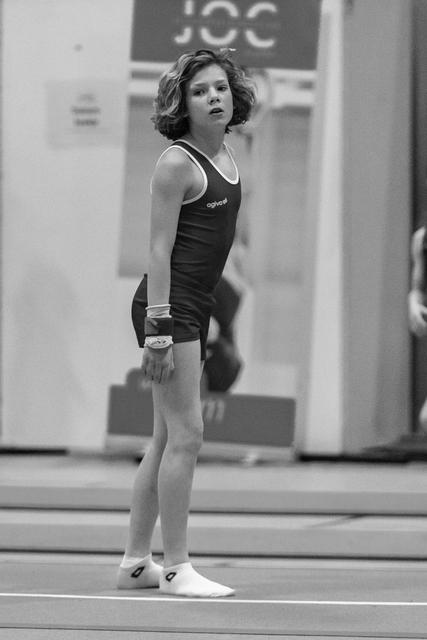 Young gymnast in black leotard stands focused on the floor mat, hands at sides, wearing white ankle socks