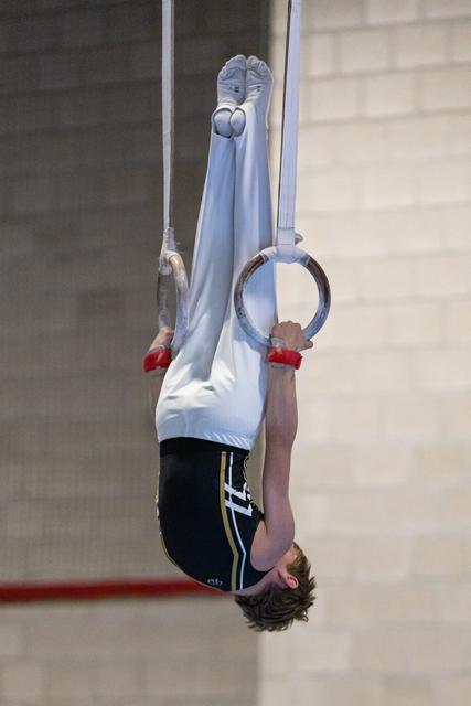 Gymnast performing an inverted hang on rings, legs extended upward, displaying strength and control during training