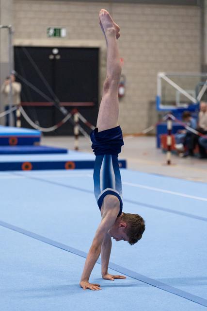 Male gymnast performing a handstand during floor exercise, demonstrating strength and balance in the training facility
