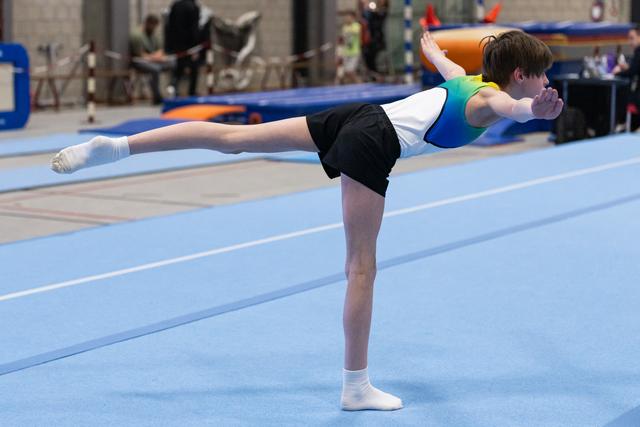 Young gymnast performing an arabesque balance on floor mat, arms positioned forward, demonstrating flexibility and control