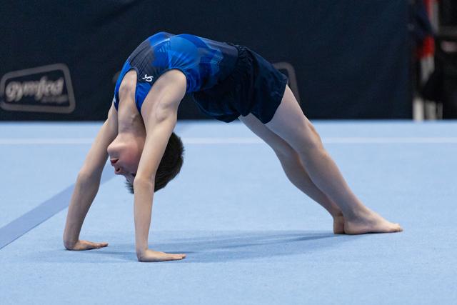Young gymnast performs a dramatic backbend bridge on the competition floor, showcasing exceptional flexibility and form