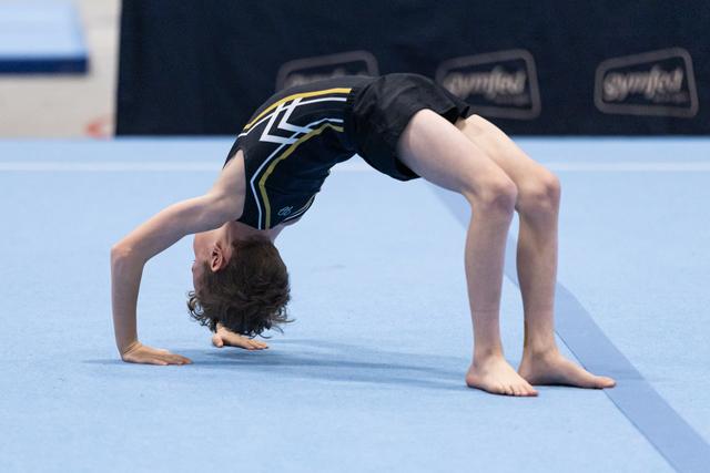 Young gymnast performs a backbend during floor routine, displaying impressive flexibility on blue mat