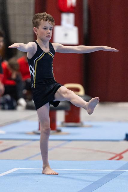 Young gymnast holds a one-legged balance with arms extended during floor routine, displaying focus and poise