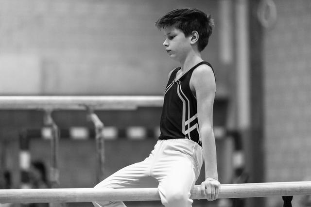 Young gymnast in black and white attire grips the parallel bar with focused concentration during routine