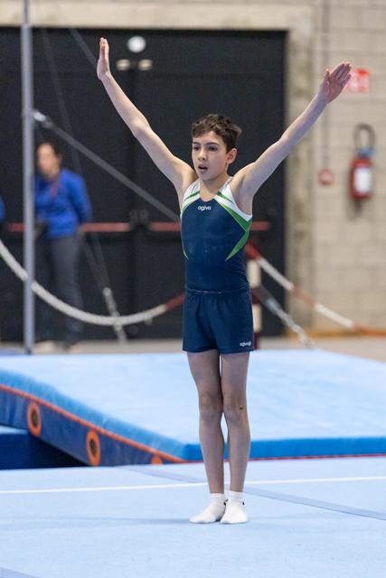 Young gymnast in blue leotard completes floor routine with arms raised high, displaying concentration and poise in training facility
