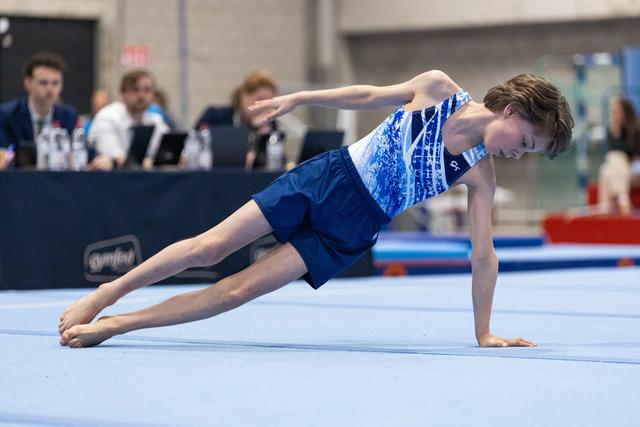 Young male gymnast performs a one-armed plank position during floor exercise routine at indoor gymnastics meet