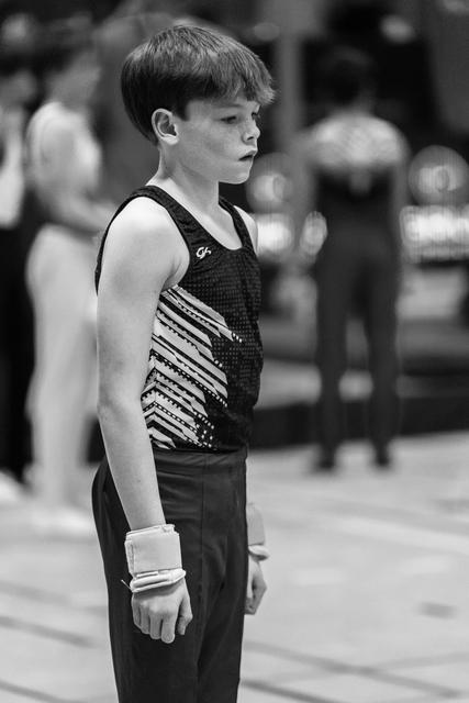 Young male gymnast stands ready with wrist supports, wearing sequined leotard, showing intense focus before his performance