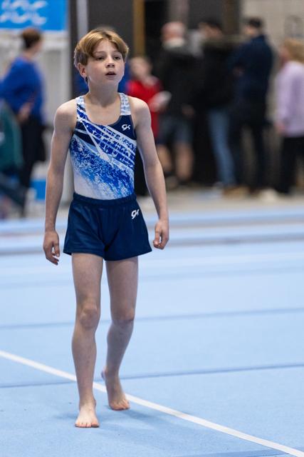 Young gymnast in blue gradient leotard stands barefoot on floor mat with concentrated expression during routine