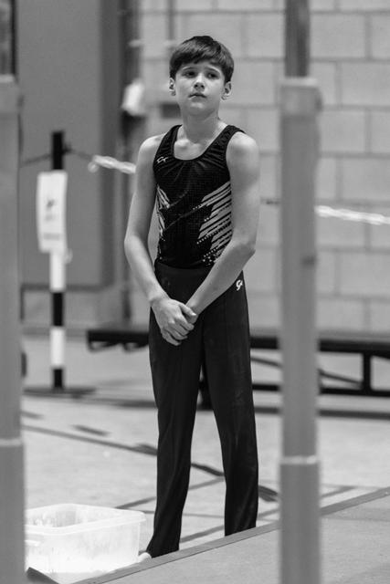 Young gymnast stands with concentrated expression and composed posture on mat, hands clasped, preparing for routine in gym