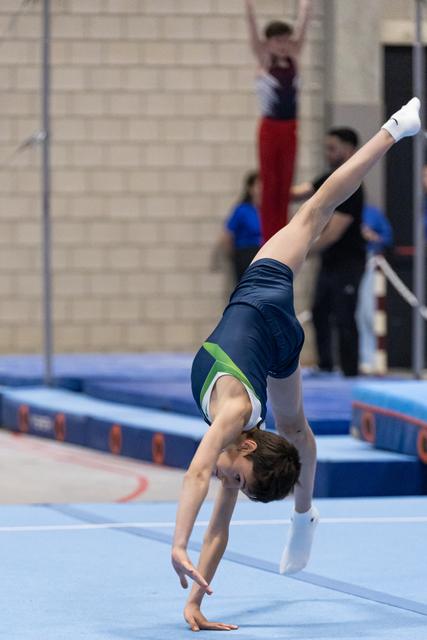 Young gymnast performs a one-armed handstand during floor routine, demonstrating strength and balance on the blue mat.