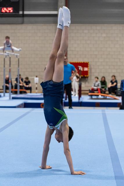 Young gymnast performs a handstand during floor exercise, legs extended vertically with pointed toes in competition setting