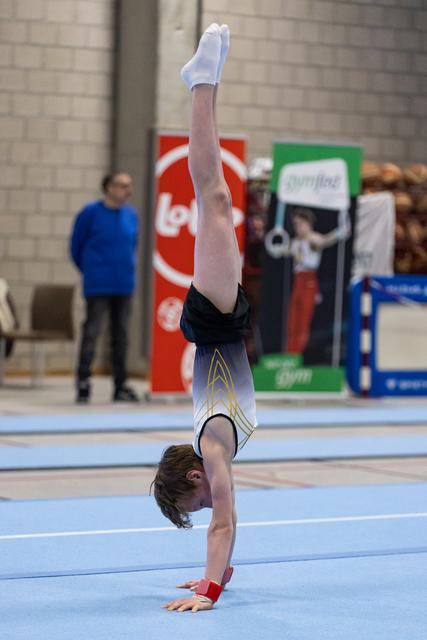Young gymnast performing a vertical handstand on floor exercise mat, demonstrating strength and balance during routine