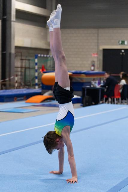 Young gymnast performing a handstand on the floor exercise mat, legs straight and pointed upward in a training facility