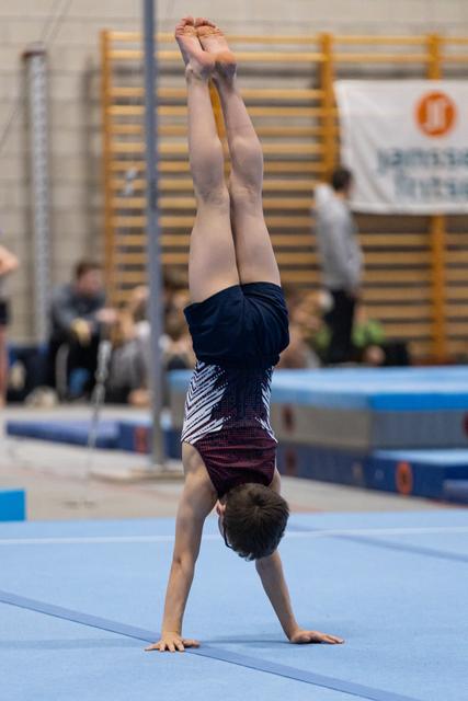 Young gymnast performs a vertical handstand on floor exercise mat, demonstrating strong balance and form during training